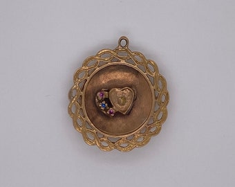 Puede incluir: Un colgante dorado con un diseño intrincado. El colgante presenta un corazón con el número "5" en su interior, rodeado de una corona de pequeñas piedras preciosas rosas y azules.