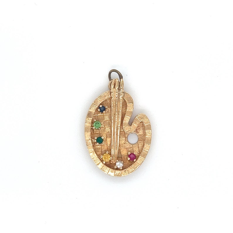Puede incluir: Encanto de paleta de artista dorado con un pincel y piedras preciosas de colores. La paleta es de forma ovalada con un peque&ntilde;o agujero en la parte superior para colgar.