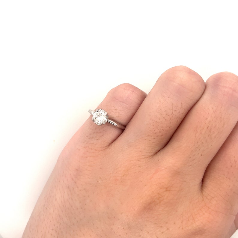 May include: A silver solitaire engagement ring with a round diamond set in a prong setting.
