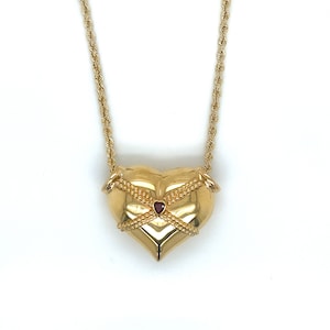 May include: A gold heart-shaped pendant necklace with a small red heart in the centre. The necklace has a rope chain.