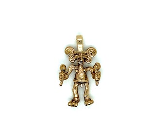 May include: A gold-coloured pendant depicting a stylised figure holding two maracas. The figure has large, round ears and a detailed face. The pendant has a loop at the top for a chain.