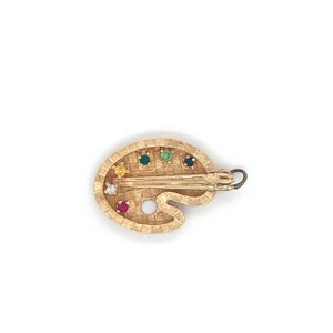 Puede incluir: Encanto de paleta de artista dorado con una superficie texturizada y piedras preciosas de colores. El encanto presenta un peque&ntilde;o detalle de pincel y un bucle para sujetarlo a un collar o pulsera.