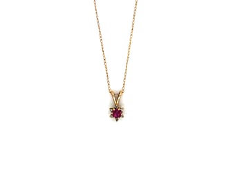 Puede incluir: Un delicado collar de oro con un pequeño colgante en forma de estrella. El colgante presenta una vibrante gema roja en el centro, rodeada de piedras más pequeñas y transparentes. La cadena es fina y elegante, adecuada para el uso diario.