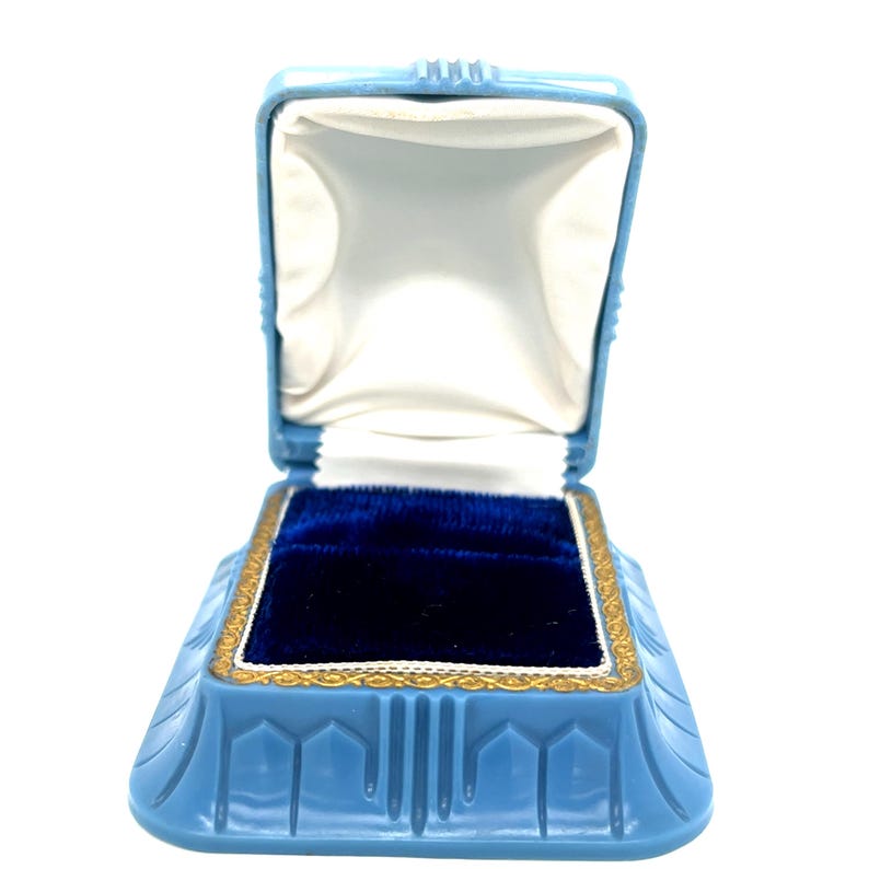 May include: A light blue, open jewelry box with a white satin interior and a deep blue velvet base. The box has a gold trim and a geometric design on the exterior.