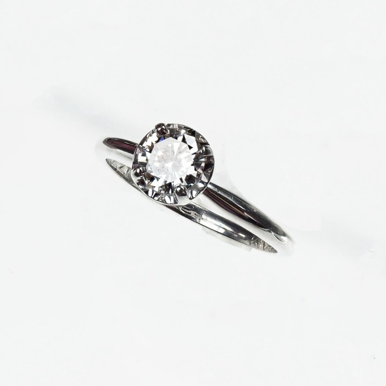 May include: A silver ring with a single round, clear gemstone set in a prong setting.