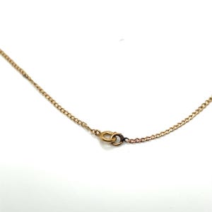 May include: Close-up of a gold-colored chain necklace with a small clasp. The chain has a delicate, linked design. The clasp is a small, circular design. The necklace is set against a white background.