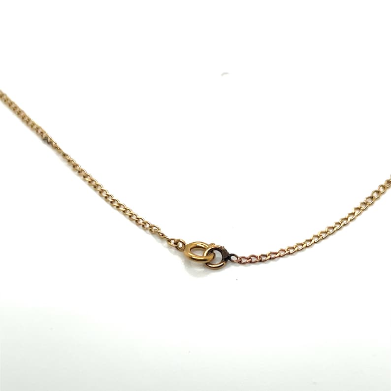 May include: Close-up of a gold-colored chain necklace with a small clasp. The chain has a delicate, linked design. The clasp is a small, circular design. The necklace is set against a white background.