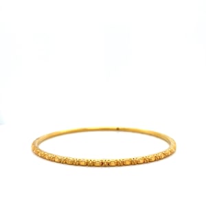 K&ouml;nnte beinhalten: Ein goldener Armreif mit einem sich wiederholenden Muster aus kleinen, erhabenen ovalen Formen. Das Armband hat eine helle, gl&auml;nzende Goldfarbe und ist vor einem wei&szlig;en Hintergrund platziert. Der Schmuck ist schlicht und elegant.