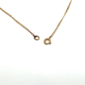 May include: A gold-colored necklace chain with a lobster clasp and a small ring on the other end. The chain is made of small, connected links. The background is white.