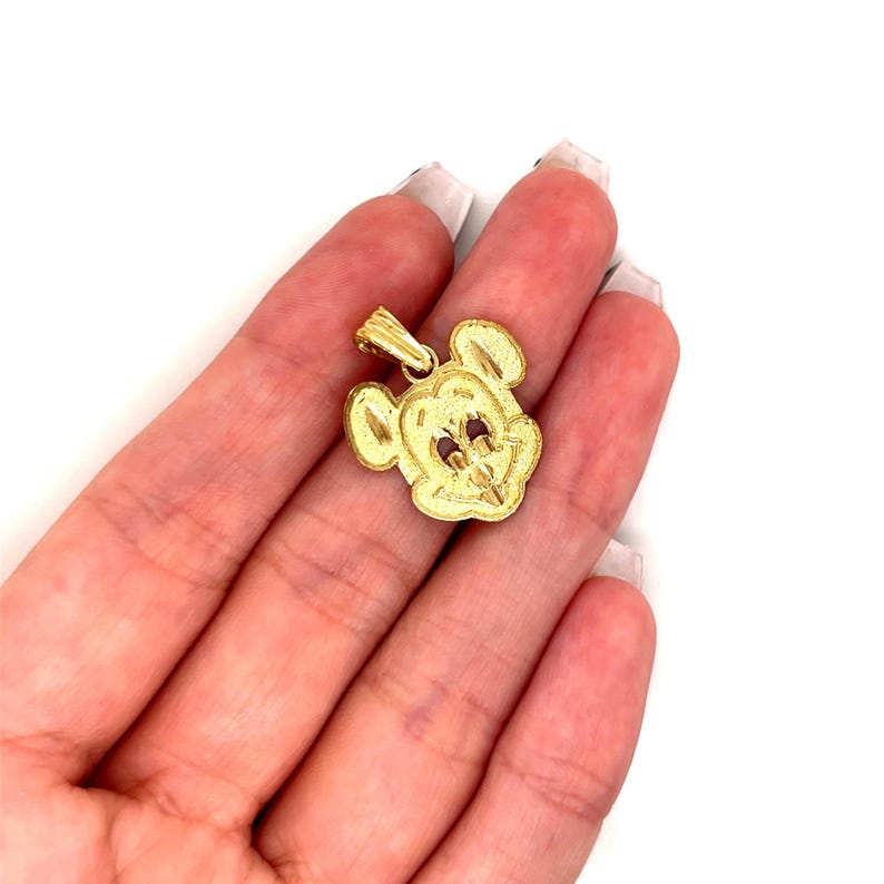 K&ouml;nnte beinhalten: Ein goldfarbener Anh&auml;nger in Form von Mickey Mouses Gesicht. Der Anh&auml;nger hat eine strukturierte Oberfl&auml;che und kleine rote Akzente f&uuml;r die Augen. Die &Ouml;se ist oben am Kopf befestigt.