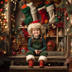 May include: A young child wearing a red and white Santa hat and a green and blue overall sits on a wooden step in front of a Christmas-themed backdrop. The backdrop features a wooden shelf with stockings and other Christmas decorations.