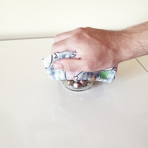 Peut inclure: Une main tenant un tissu à carreaux bleus et blancs sur un bocal en verre rempli de bonbons colorés.
