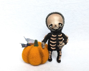 May include: A handmade Halloween-themed felt figure of a skeleton in a black suit with bone accents, standing next to an orange pumpkin. A butterfly rests on the pumpkin. The skeleton has a skull-shaped head and is posed as if it is standing.