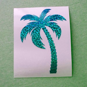 Peut inclure: Un autocollant en forme de palmier scintillant turquoise sur fond blanc. Le motif du palmier est une silhouette à l'aspect texturé et scintillant. L'autocollant est rectangulaire et posé sur une surface vert clair.