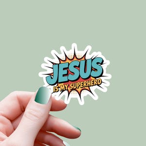 Puede incluir: Una pegatina con el texto "JESUS IS MY SUPERHERO" en estilo cómic. La palabra "JESUS" es azul con contorno negro, y el texto "IS MY SUPERHERO" es amarillo. La pegatina tiene un borde blanco y un diseño de estrella.