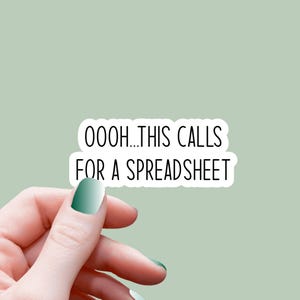 Può includere: Un adesivo bianco con la scritta "OOOH...THIS CALLS FOR A SPREADSHEET" in nero, tenuto in mano con unghie verdi sfumate su sfondo verde chiaro. L'adesivo è rettangolare con angoli arrotondati.