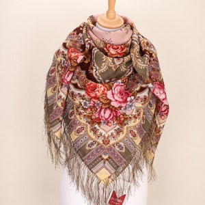 Może przedstawiać: Tradycyjny rosyjski szal z kwiatowym wzorem w odcieniach różowego, czerwonego i zielonego. Szal ma brązową frędzlę i jest prezentowany na białym manekinie.