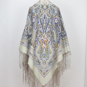 Może przedstawiać: Jasno błękitny i zielony wzorzysty szal z wzorem paisley i frędzlami. Szal jest prezentowany na drewnianym manekinie.