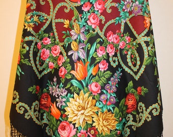May include: A floral shawl with a black fringe. The shawl features a vibrant design of roses, tulips, and other flowers in shades of pink, red, yellow, and purple. The background is a mix of red and black.