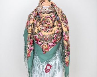 May include: A green and yellow floral patterned shawl with fringe. The shawl is displayed on a wooden mannequin.