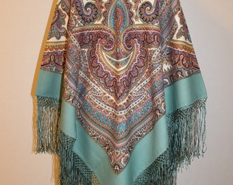 May include: A teal blue paisley patterned shawl with fringe. The shawl has a white background with a large paisley design in the center.