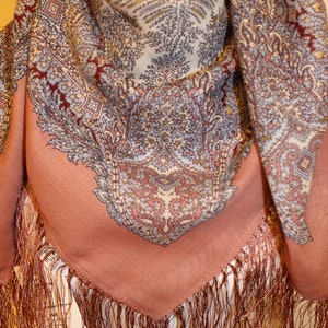 Może przedstawiać: Szal w wzór paisley na brzoskwiniowym tle z brązowymi frędzlami. Szal jest złożony na pół i ma białą podszewkę.