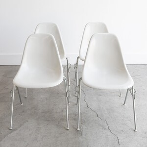 May include: Four white plastic chairs with chrome legs. The chairs are arranged in a row, facing the camera.
