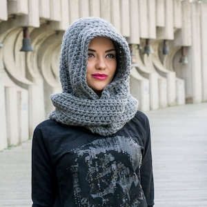 May include: A woman wearing a gray crocheted hooded scarf with a black long-sleeved shirt that has a sequined graphic of a skull with the text "Only The Brave" on it.
