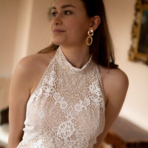 May include: A white lace halter top with a high neckline and a scalloped hem. The top is sheer and has a delicate floral pattern.