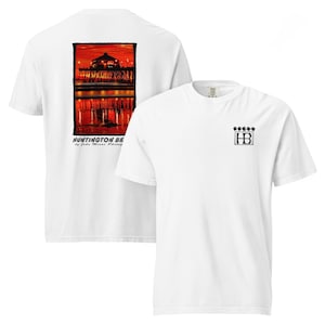 Op de afbeelding: Witte T-shirts. Eén heeft een zonsondergangscène van Huntington Beach, Californië, met de tekst "Huntington Beach" en de naam van een fotograaf. De andere heeft een klein zwart logo met de letters "HB" en vijf sterren.