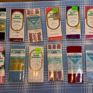 May include: Assortment of vintage seam binding packages in various colors, including black, rust, pink, blue, and white. The packages feature text such as "Stretch Lace" and "Seam Binding J&P Coats."