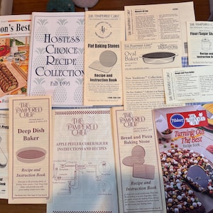 May include: A collection of vintage recipe books and instruction manuals from The Pampered Chef and Pillsbury. Titles include "Season's Best," "Hostess Choice Recipe Collection," and "Turning Out The Best Recipe Book." Various kitchen tools are also featured.