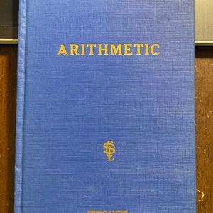 Puede incluir: Un libro de tapa dura azul con el título "Arithmetic" en letras doradas. El libro tiene un símbolo dorado y la palabra "Pergande" impresa en la portada.