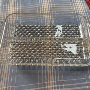 May include: A clear, rectangular glass serving dish with two compartments. The dish has a textured, bubble-like pattern on the bottom and decorative handles on each end. Ideal for serving appetizers or snacks.
