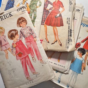 Może przedstawiać: Kolekcja starych wykrojów krawieckich z ilustracjami sukienek, kombinezonów i innych ubrań. Wzory pochodzą od marek takich jak Simplicity i McCall's, z widocznymi cenami i rozmiarami.