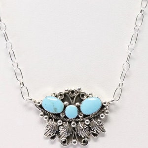 May include: A silver necklace featuring a pendant with three oval turquoise stones. The pendant has a decorative silver filigree design with leaf and bead accents, and is suspended from a silver chain.