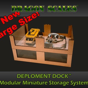 May include: A two-tiered cardboard storage system with clear plastic windows. The system is labeled "DEPLOYMENT DOCK™ Modular Miniature Storage System". The top tier contains a yellow toy vehicle and the bottom tier contains a gray toy vehicle. The text "New Large Size!" is in red letters on a green background.