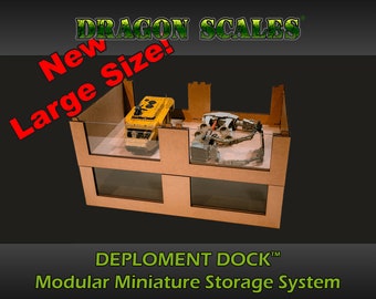 May include: A two-tiered cardboard storage system with clear plastic windows. The system is labeled "DEPLOYMENT DOCK™ Modular Miniature Storage System". The top tier contains a yellow toy vehicle and the bottom tier contains a gray toy vehicle. The text "New Large Size!" is in red letters on a green background.