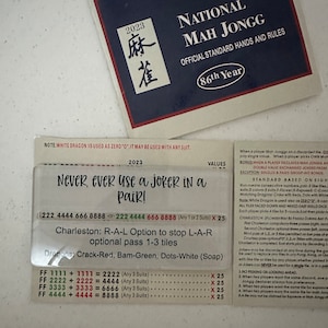 May include: A close-up of a Mah Jongg rule sheet with the text "Never, ever use a joker in a pair!" and a table of point values for different hand combinations. The sheet is blue and white with the text "National Mah Jongg" and "86th Year" at the top.