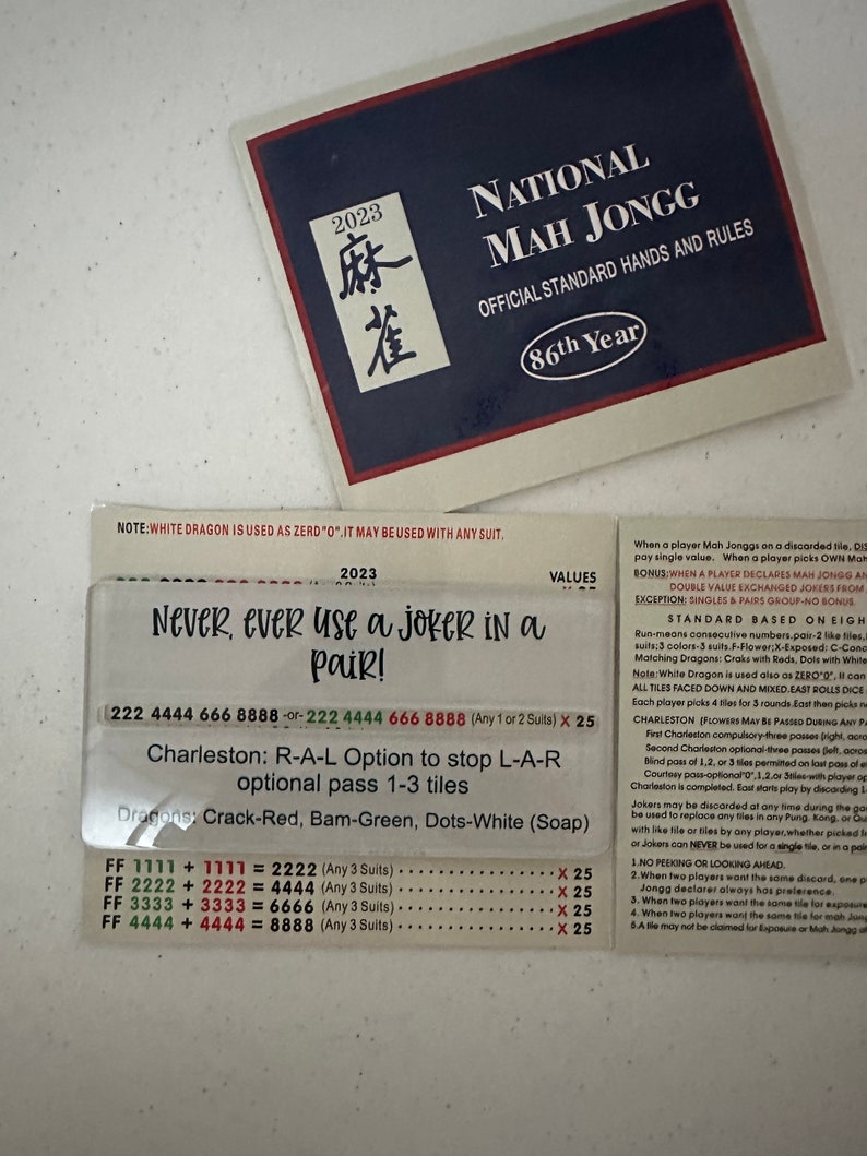 May include: A close-up of a Mah Jongg rule sheet with the text "Never, ever use a joker in a pair!" and a table of point values for different hand combinations. The sheet is blue and white with the text "National Mah Jongg" and "86th Year" at the top.