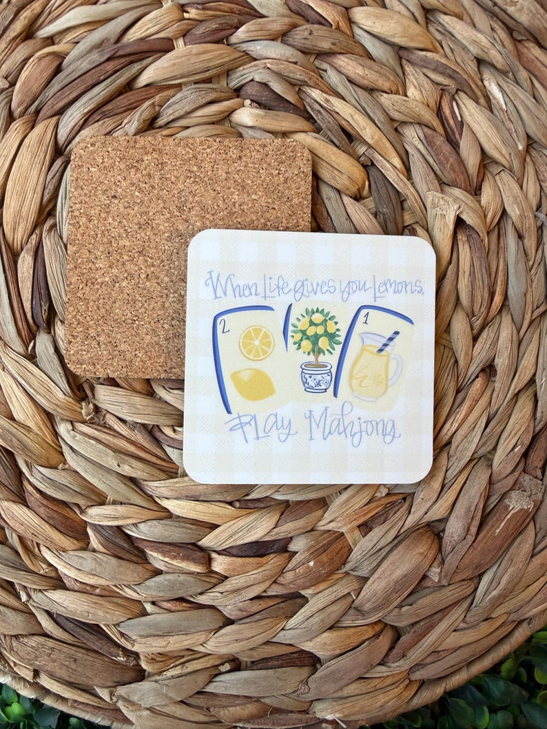 May include: A square coaster with a cork backing and a white surface featuring a light yellow gingham pattern. The design includes illustrations of a lemon, a lemon tree, and a pitcher of lemonade, with the text When Life gives you Lemons, Play Mahjong.