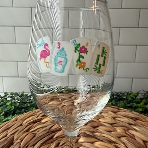 Pode incluir: Uma ta&ccedil;a de vinho de vidro transparente com quatro autocolantes coloridos de pe&ccedil;as de Mahjong. Os desenhos incluem um flamingo cor-de-rosa com a palavra East, um frasco de gengibre azul e branco com o n&uacute;mero 3, flores com o n&uacute;mero 2 e bambu verde com o n&uacute;mero 4.