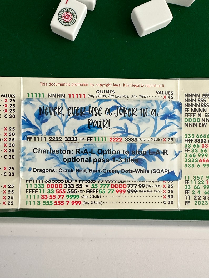 May include: A close-up of a game board with instructions for playing a game called "Charleston". The board is green and has a white border. The instructions are written in black and red text. The text includes the phrase "Never, ever use a joker in a pair!" and the words "Dragons: Crack-Red, Bam-Green, Dots-White (SOAP)".