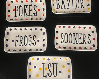 May include: Five rectangular white ceramic trays with black text and colorful polka dots. The trays display the names "POKES", "BAYLOR", "FROGS", "SOONERS", and "LSU". Each tray has a different team name.