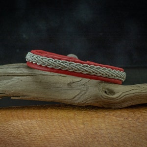 May include: A red leather bracelet with a silver braided design.