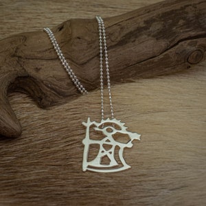 Puede incluir: Un collar de plata con un colgante con un diseño abstracto. El colgante es un recorte de una figura estilizada con un ojo circular y formas geométricas.