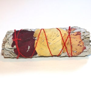 以下が含まれることがあります： 赤い紐で包まれ、赤、黄、オレンジの色合いの乾燥した花びらで飾られた白いセージのスマッジスティックです。