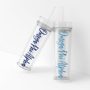 May include: Two clear plastic tumblers with straws. The tumbler on the left has "Omega Phi Alpha" written in blue lettering. The tumbler on the right has "Omega Phi Alpha" written in light blue lettering.