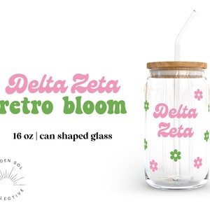 May include: A 16 ounce glass can-shaped tumbler with a pink and green "Delta Zeta retro bloom" design and a green straw.