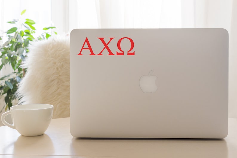 May include: A white laptop computer with a red "AXO" sticker on the back. The laptop is sitting on a light wood surface.
